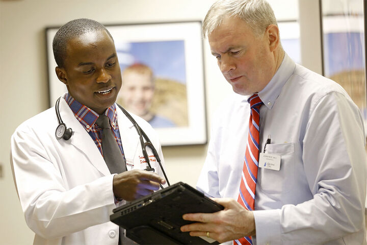 A physician holds a tablet as a medical student points to the screen.